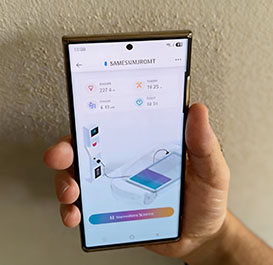 Mano che tiene uno smartphone con lo schermo acceso su un'applicazione che mostra i dati in tempo reale e lo stato di carica di una colonnina per veicoli elettrici.